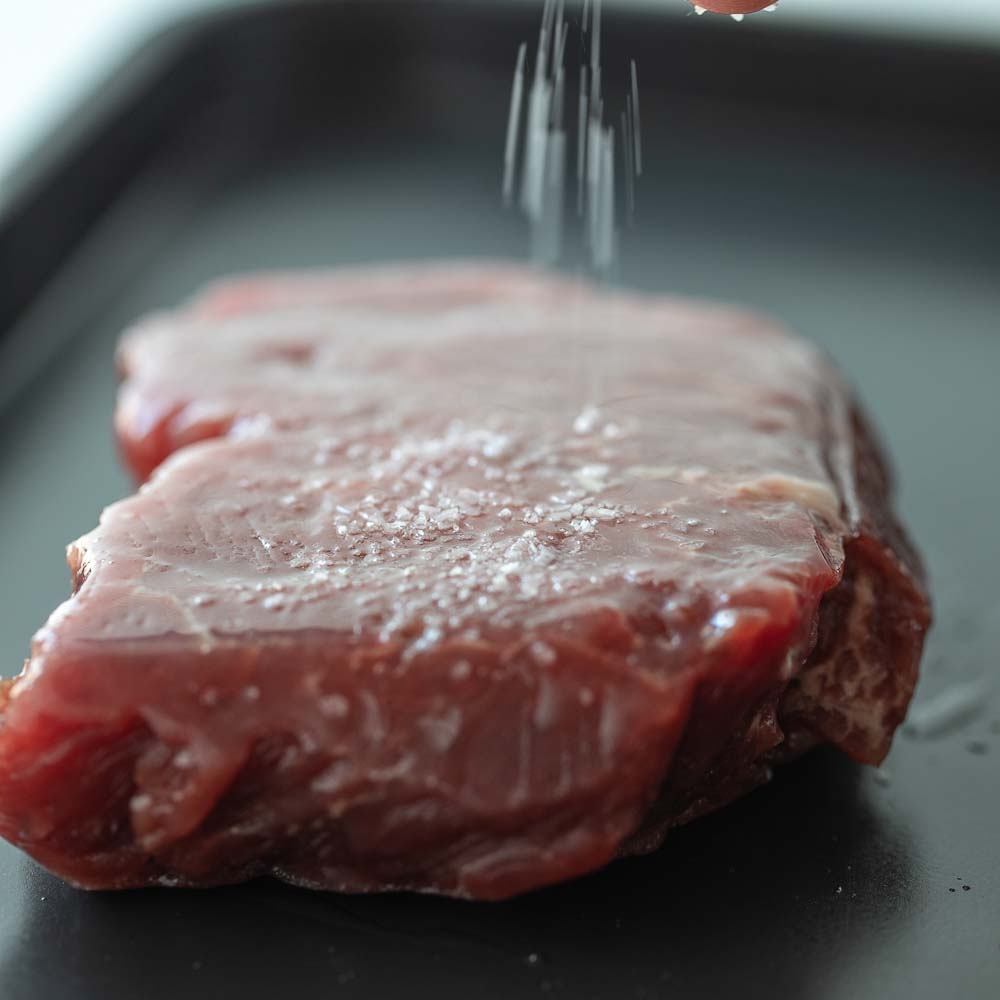 A frozen steak being salted.