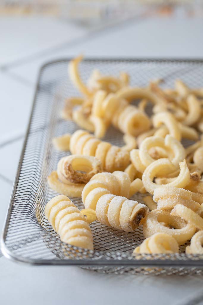 A close up of air fried curly fries on an air fryer wire pan before cooking.