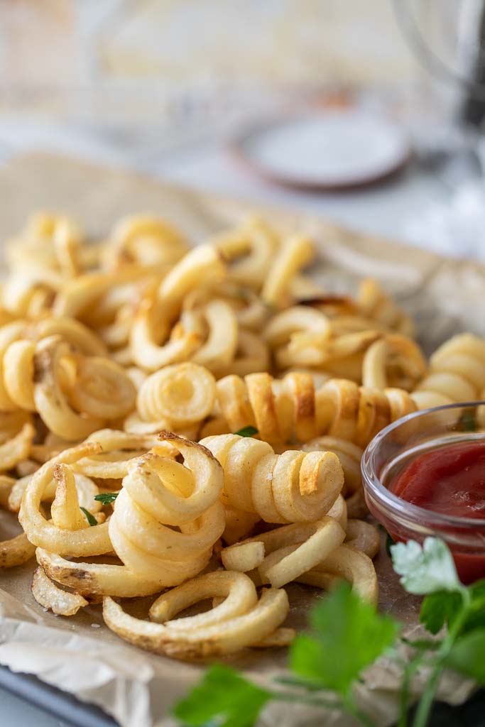 A close up of air fried curly fries next to a container of ketchup.