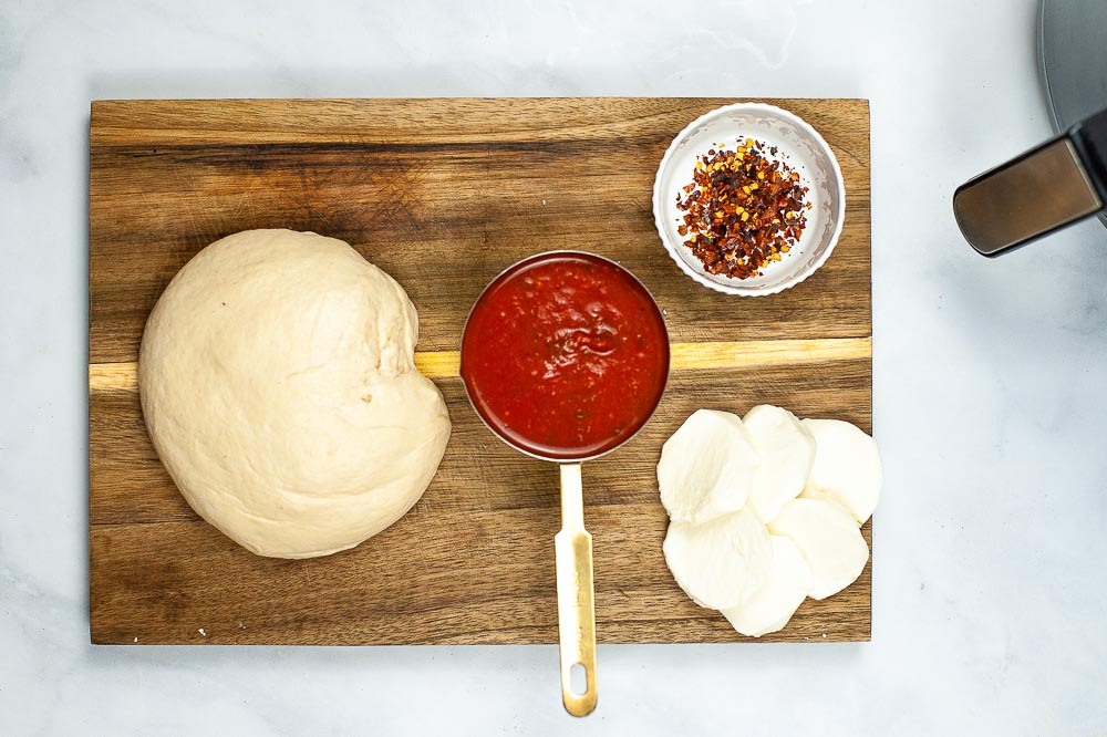 Ingredients for homemade air fryer pizza on a wooden cutting board.