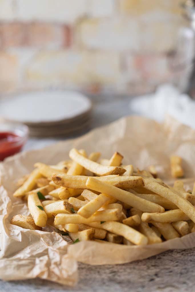 A close up of air fried french fries on a table on crinkled parchment paper.