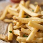 A close up of air fried french fries on a table with ketchup.