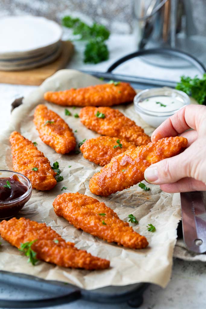 a hand taking a sauced buffalo chicken tender