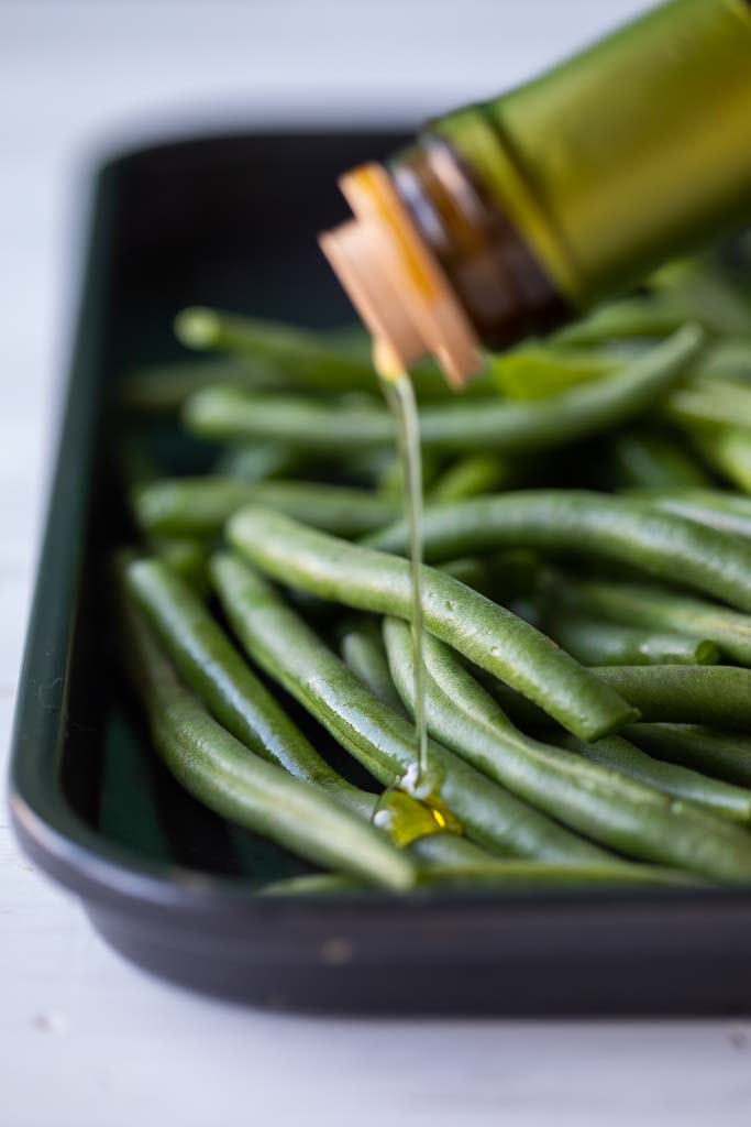 Oil being drizzled over fresh green beans.